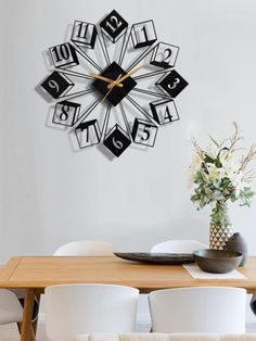 a clock that is on the wall above a dining room table with white chairs and a vase