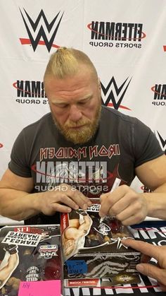 a man sitting at a table signing autographs for people to sign on his shirt