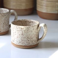 two coffee mugs sitting next to each other on a white counter top with brown speckles