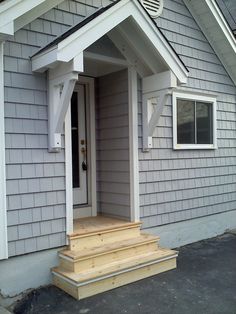 the front door of a gray house with white trim and wooden steps leading to it