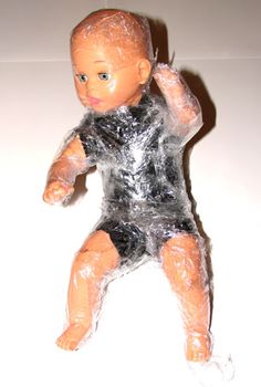 a plastic baby doll wrapped in plastic on a white surface with water all over it's body