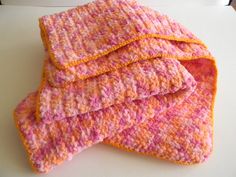 three pink and orange crocheted dishcloths sitting on top of a table