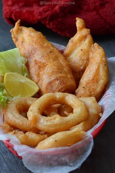 fried fish and onion rings in a basket with lime wedges next to it on a table