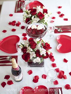 the table is set with red and white flowers, silverware, and wine glasses