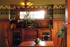 a wooden dining room table and chairs in front of a window with green wallpaper