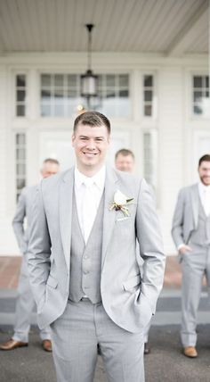 a group of men standing next to each other in front of a white building and wearing suits