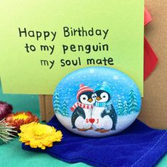 a penguin painted on a rock next to flowers and a sign that says happy birthday to my penguin my soul mate