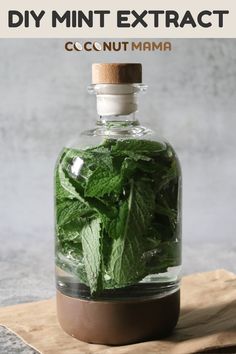 a bottle filled with green leaves on top of a wooden table