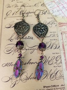 30x21mm fancy bronze shield link. 20x9mm pressed Czech glass patterned oval, blue opal picasso pink wash. 10 & 4mm faceted glass rounds plum. 4mm corrugated metal spacers. Antique bronze bead caps and fishhook ear wires. Antique Purple Metal Jewelry, Purple Wire Wrapped Czech Glass Jewelry, Bronze Czech Glass Drop Earrings, Bronze Czech Glass Jewelry With Ear Wire, Handmade Bronze Jewelry With Czech Glass, Handmade Czech Glass Bronze Jewelry, Nickel-free Czech Glass Artisan Jewelry, Artisan Nickel-free Czech Glass Jewelry, Artistic Jewelry With Czech Glass And Ear Wire