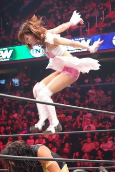 a woman in white dress standing on top of a rope next to a crowd at a wrestling match