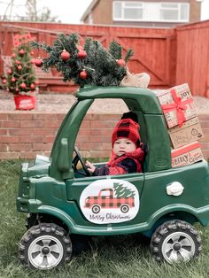 a small child in a green truck with christmas trees on top