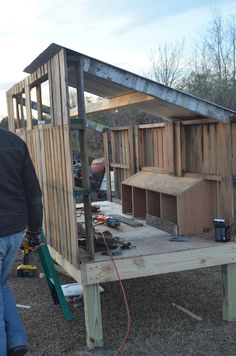 a man standing in front of a wooden structure that has been built into the ground