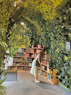 a woman standing in front of a bookshelf filled with lots of green plants