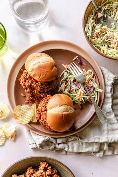 two sloppy joe sandwiches on a plate with coleslaw and chips next to it