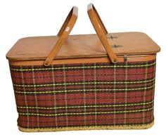 a brown and yellow plaid picnic basket with two wooden handles on the front, sitting against a white background