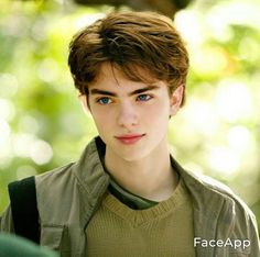 a young man with blue eyes looks at the camera while standing in front of trees