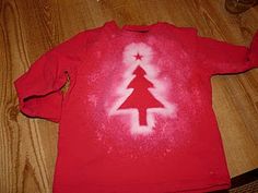 a red shirt with a white christmas tree on the front and bottom, sitting on a wooden floor