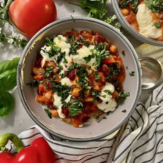 two bowls filled with food sitting on top of a table next to tomatoes and other vegetables