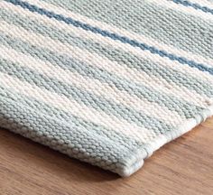 a close up of a rug on a wooden floor with a white and blue striped design