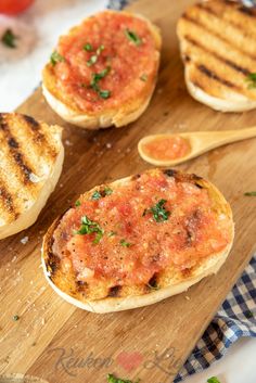 three grilled sandwiches with tomato sauce and parsley on a cutting board next to a wooden spoon