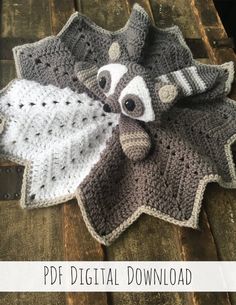 a crocheted raccoon is laying on top of a wooden table with a white and gray blanket