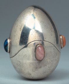 a silver object with a pink and blue decoration on the front, sitting on a gray surface