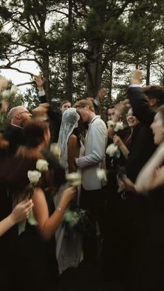 a group of people standing around each other with flowers in front of them and one person kissing the woman