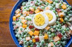 a blue bowl filled with peas, hard boiled eggs and bacon bits on top of it