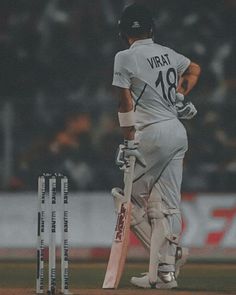 a man standing next to a cricket ball on top of a field holding a bat