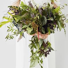 a woman holding a bouquet of greenery in her hands