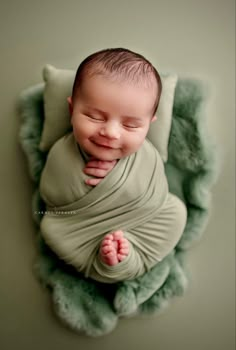 a baby wrapped in a blanket is smiling and laying on its back with his hands under his chin