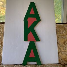 a green and red wooden sign sitting on top of a white wall next to a window