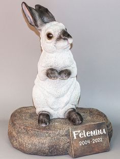 a figurine of a rabbit sitting on top of a rock with a name plate