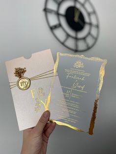 a person holding up a silver and gold wedding card in front of a clock tower