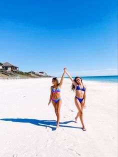 two women in bikinis standing on the beach with their hands up to each other