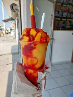 a person holding up a large cup filled with ice cream and fruit toppings on the outside of a building