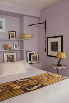 a bedroom with purple walls and pictures on the wall above the bed, along with two lamps