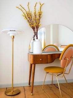 a desk with a mirror, chair and vase on it next to a table lamp