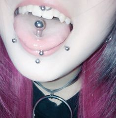 a woman with pink hair has piercings on her nose and tongue, while wearing a black shirt