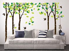 a living room with white couches and green trees on the wall behind it,