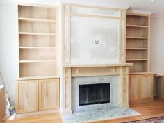 an empty living room with a fireplace and built in bookshelves