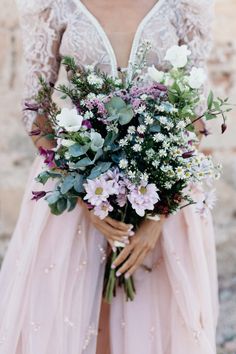 a woman holding a bouquet of flowers in her hands and wearing a dress with sheer sleeves