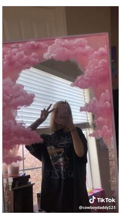 a woman taking a selfie in front of a mirror with pink clouds on it