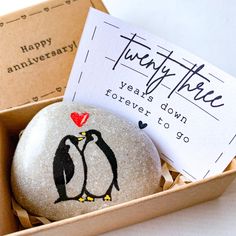 a rock with a penguin painted on it in a box next to a card that says twenty three years down forever to go