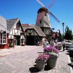 people are walking around in front of windmills and buildings with flower pots on the sidewalk