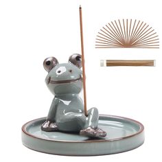 a frog figurine sitting on top of a saucer with a stick in it's mouth