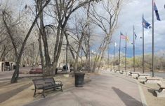 an empty park with benches and flags on the side walk next to trees that have no leaves