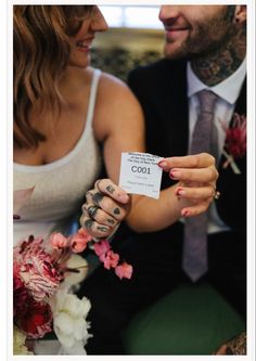 a man and woman sitting next to each other with tattoos on their arms holding a card