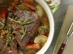 a pot filled with meat and vegetables on top of a table next to utensils