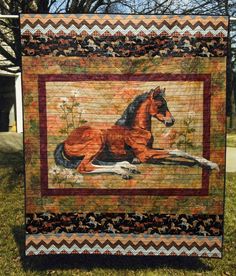 a quilt with a horse on it is hanging in front of some trees and grass